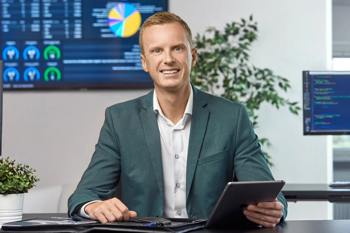 Mand i blågrøn blazer holder en tablet ved et skrivebord i et moderne kontor.